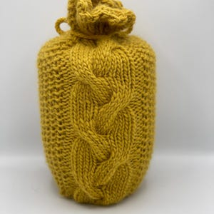 Op de afbeelding: Een gele gebreide flessenwarmer met een kabelbreipatroon.