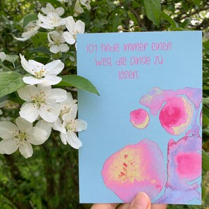 May include: A light blue card with pink and yellow watercolor splotches. The card has the text "Ich finde immer einen Weg, die Dinge zu l&ouml;sen." in pink lettering.