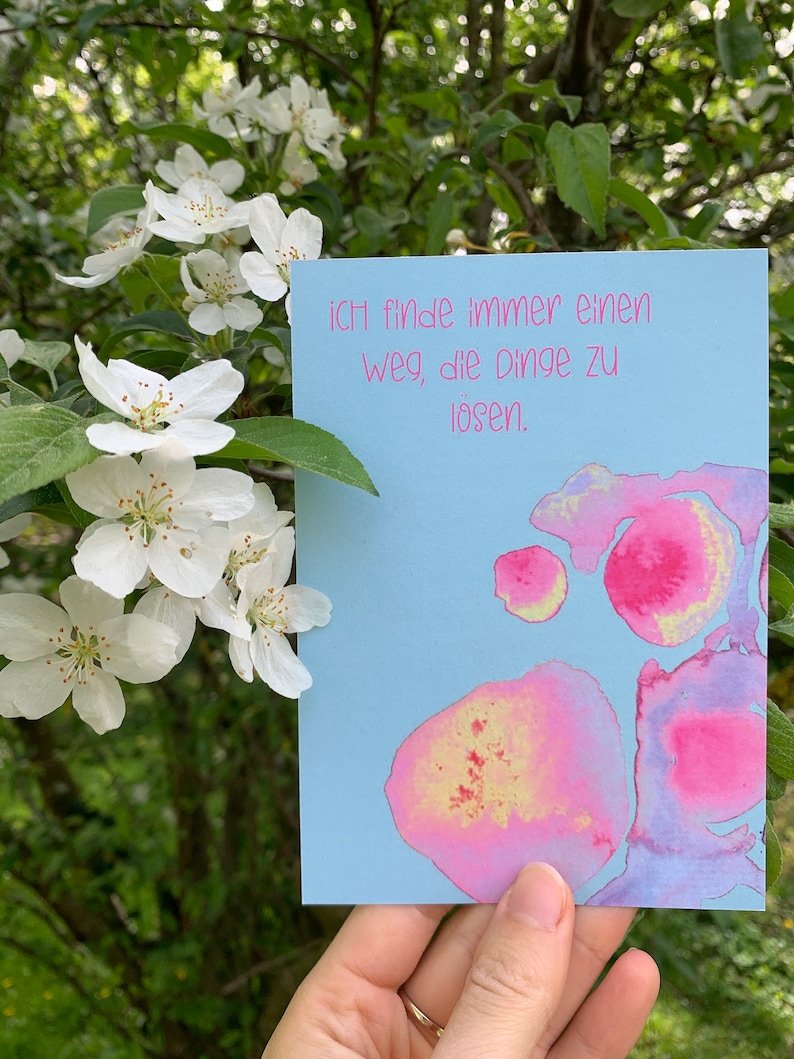 May include: A light blue card with pink and yellow watercolor splotches. The card has the text "Ich finde immer einen Weg, die Dinge zu l&ouml;sen." in pink lettering.