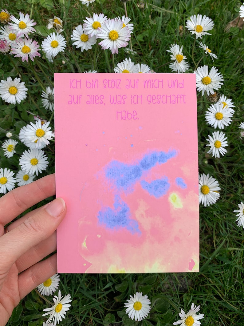 May include: A pink card with a blue and yellow watercolor design. The card has the text "Ich bin stolz auf mich und auf alles, was ich geschafft habe." written in black ink.