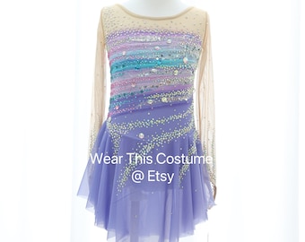 Può includere: Un abito da pattinaggio artistico di colore lavanda con un design sfumato arcobaleno e decorazioni di cristalli. L'abito ha maniche lunghe e una gonna di tulle. Il testo "Wear This Costume @ Etsy" è stampato sulla gonna.