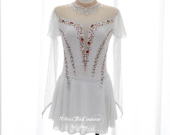 May include: A white figure skating dress with long sleeves and a sheer overlay. The dress is decorated with rhinestones in a geometric pattern, including red, yellow, and clear stones. The dress has a V-neckline and a skirt with a scalloped hem. The text "Wear This Costume @Etsy" is visible on the skirt.