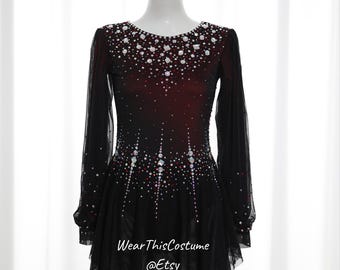 May include: A black and burgundy figure skating dress with long sleeves and a sparkling rhinestone design. The dress has a fitted bodice and a flared skirt with a layered, asymmetrical hem.