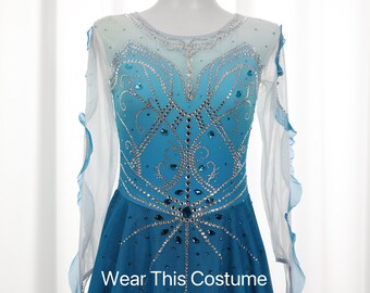 May include: A blue and white figure skating dress with a crystal design and a ruffled sleeve. The dress has a gradient design that fades from white to blue. The skirt is a ruffled design. The dress is on a mannequin. "Wear This Costume @Etsy" is written on the dress.