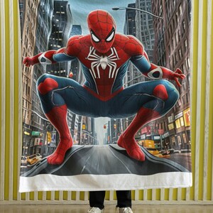 Puede incluir: Una manta de forro polar blanca con una imagen impresa de Spider-Man con un traje rojo y azul, de pie en una calle de la ciudad. El fondo es una ciudad con edificios altos.