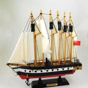 May include: A detailed wooden model of a sailing ship, featuring white sails, a black and red hull, and a Union Jack flag. The model has multiple masts and rigging, and is mounted on a black base with "GREAT BRITAIN".