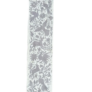 Puede incluir: Un camino de mesa de lino blanco con un diseño bordado gris de pájaros, flores y animales. El diseño es arte popular mexicano tradicional.