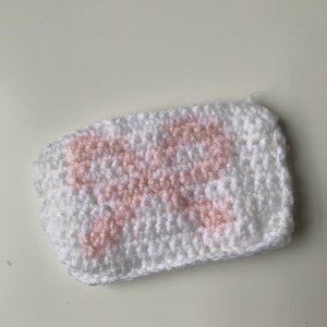 May include: A white crocheted pouch with a pink crocheted design. The pouch is small and has a rectangular shape.