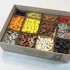 May include: A wooden box containing a variety of coloured wooden game pieces, including orange, yellow, brown, grey, white and black. The box is labelled "Caverna: The Cave Farmers".