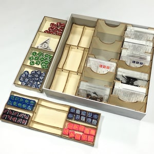 Könnte beinhalten: Ein Holzorganizer mit mehreren Fächern zum Verstauen von Spielsteinen und Karten. Der Organizer hat eine weiße Außenseite und ist mit verschiedenen farbigen Würfeln und Karten gefüllt.