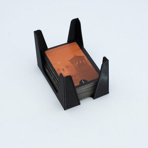 Könnte beinhalten: Schwarzer Plastikkartenhalter mit einem Stapel Karten darin. Die oberste Karte zeigt ein Gebäude mit rotem Himmel.