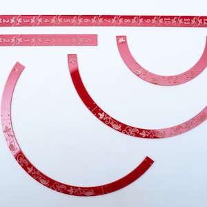 Puede incluir: Cuatro piezas de papel semicirculares rojas y rosadas con un diseño floral y los números del 1 al 12 impresos en ellas.