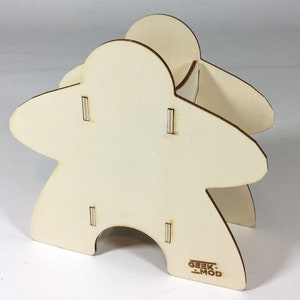 May include: A wooden game organizer shaped like a  classic game piece. The organizer has four slots for storing game components. The organizer is made of natural wood and has a "Geek-Mod" logo on the bottom.