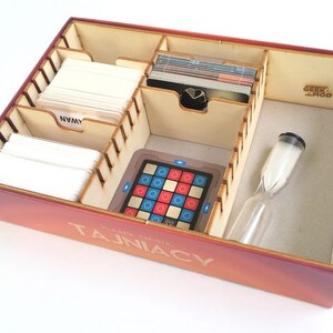 May include: A wooden game organizer insert for the board game "Tajniacy" (codenames). The insert has compartments for cards, a timer, and a game board. The insert is labeled "Geek Mod".