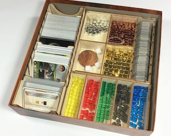 May include: A wooden box with dividers for organising game pieces and cards. The box contains a variety of coloured plastic cubes, a metal coin, and several stacks of cards. The box is labelled "KOPORACJA DLA POCZĄTKUJĄCYCH".