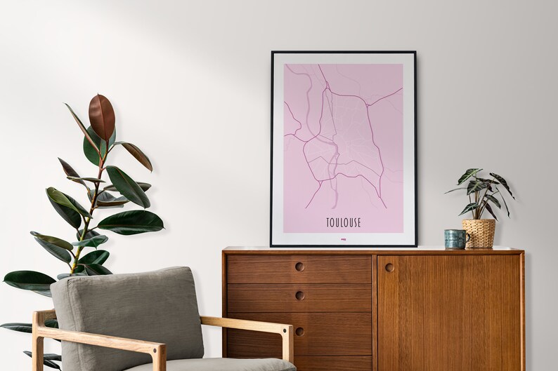 Może przedstawiać: Wzorowana mapa Tuluzy we Francji, w kolorze r&oacute;żowym, w czarnej ramie. Mapa wisi na ścianie nad drewnianym komodą z dwoma szufladami i drzwiami szafki. Na komodzie stoją dwie rośliny.