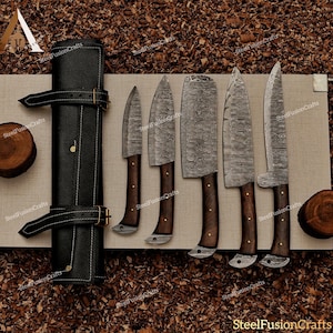 Può includere: Set di cinque coltelli da cucina con manici in legno e un rotolo in pelle nera per la conservazione. I coltelli hanno un motivo a lama in acciaio damascato.