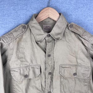 May include: A beige long-sleeved shirt with two large flap pockets and a button-up front. The shirt has a small label on the collar that reads "Japan Regulation Type".
