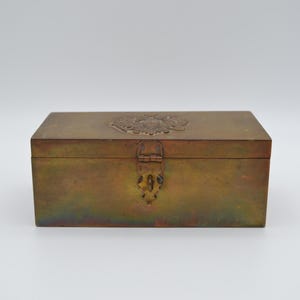 May include: A brass box with an ornate design on the lid and a hinged clasp. The box has a slightly iridescent finish.