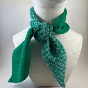 May include: A green and white patterned scarf is displayed on a mannequin. The scarf is knotted at the front, with the ends falling down. The pattern features small white designs on a green backdrop. The scarf is made of a soft, textured material, suitable for wear.