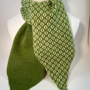May include: A green and white patterned scarf displayed on a mannequin. The scarf has a diamond pattern in white against a green background. The scarf is made of a soft, knitted material and is designed to be worn around the neck.