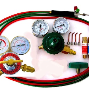 Op de afbeelding: Een gassweisset met twee drukregelaars, één met het label Acetyleen met een rode voorkant en één groene regelaar, twee sets dubbele manometers, rode en groene slangen, een toortshandgreep, vier kleine koperen tips en twee gascilinders.
