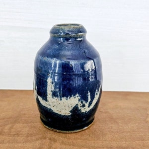 May include: A small, blue ceramic vase with white accents. The vase has a rounded body and a narrow opening.