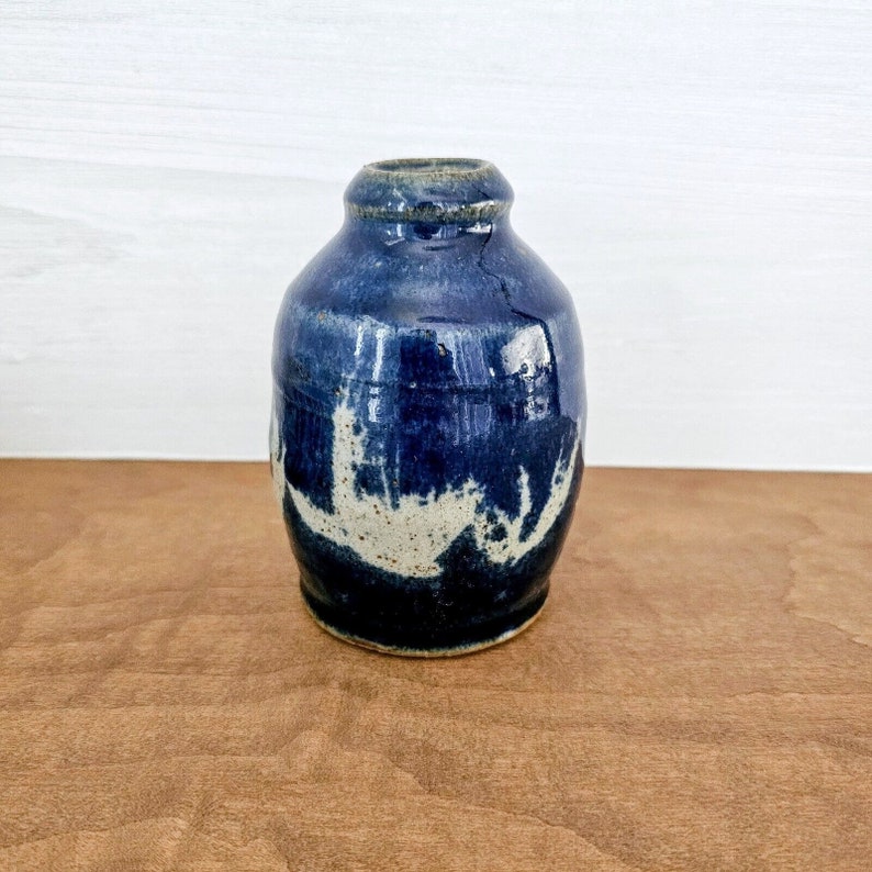 May include: A small, blue ceramic vase with white accents. The vase has a rounded body and a narrow opening.