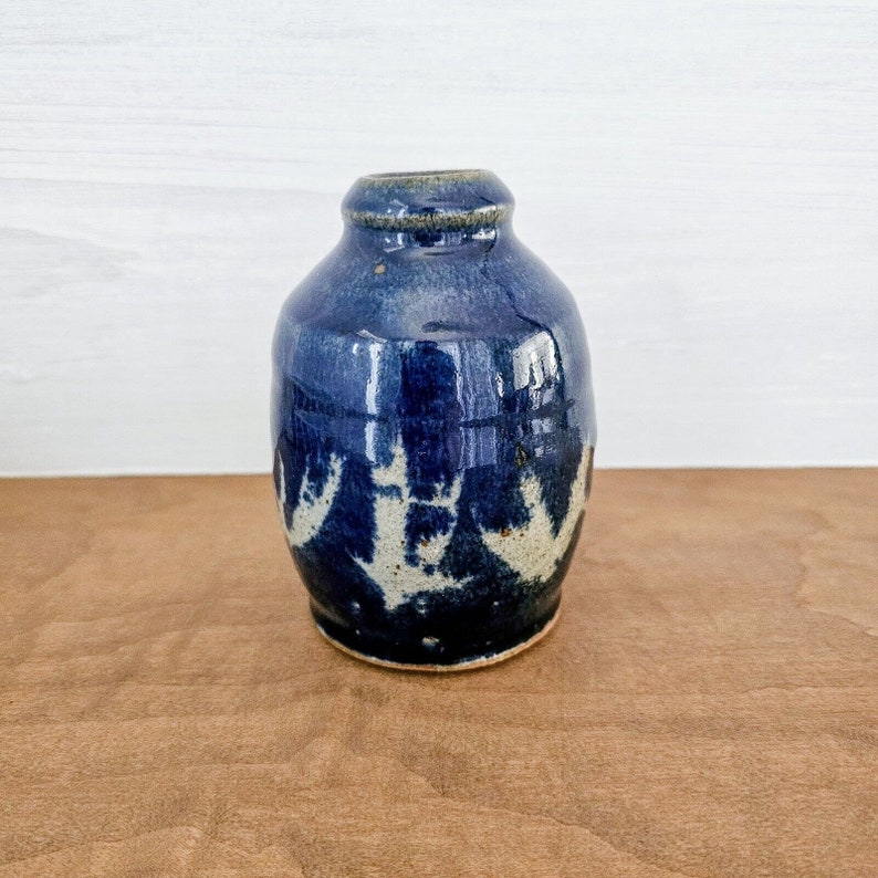 Pu&ograve; includere: Un piccolo vaso in ceramica blu con un designo bianco. Il vaso ha un corpo arrotondato e un'apertura stretta.