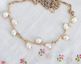 Op de afbeelding: Een gouden ketting met een delicaat takkenontwerp en nepparel accenten. De ketting ligt op een witte stoffen achtergrond.