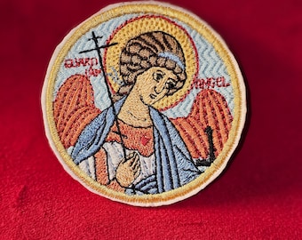 May include: Embroidered patch featuring a colorful depiction of an angel with wings, holding a cross. The angel is wearing a blue robe and has a halo. The patch has a white border and the words "GUARDIAN ANGEL" are embroidered around the edge.