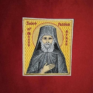 Op de afbeelding: Gestikte patch met een religieus icoon van Sint Paisios van de berg Athos. Het icoon toont een man met een baard in een zwarte robe met een witte halo. De patch is geel met een witte rand en de tekst "Sint van de berg Athos Paisios Athos" is geborduurd in rood en zwart.