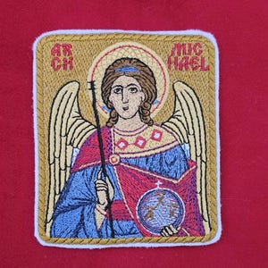 Könnte beinhalten: Gestickter Aufnäher mit einem Engel mit Heiligenschein, Flügeln und Stab. Der Engel trägt blaue und rote Gewänder und hält eine Weltkugel. Der Aufnäher hat einen goldenen Rand und die Worte "ARCH MICHAEL" stehen oben.