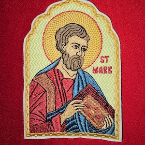 Op de afbeelding: Gestikte patch met een geel, rood en blauw icoon van Sint Marcus die een boek vasthoudt. De patch heeft een witte rand en de tekst "ST MARK" in geel.