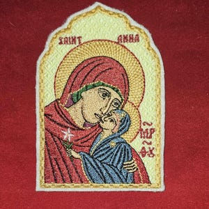 May include: Embroidered patch featuring a religious icon of a woman holding a child. The icon is surrounded by a gold frame and the words "Saint Anna" are embroidered on the top.
