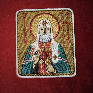 Op de afbeelding: Gestikte patch met een religieus icoon van St. Tikhon, Patriarch van Moskou. Het icoon is omgeven door een gouden frame met witte stiksels. De tekst "St. Tikhon, Patriarch van Moskou" is rondom het icoon gestikt.