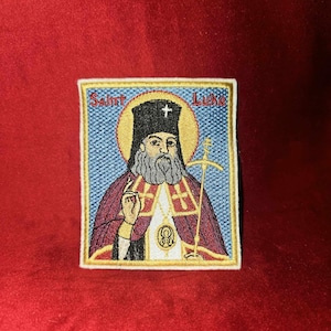 May include: Embroidered patch featuring a colorful depiction of Saint Luke, with the text "Saint Luke" above the image.