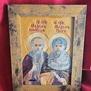 May include: Embroidered religious icon featuring two figures with long beards and halos, set within a distressed wooden frame. The figures are depicted in detailed embroidery with vibrant colors. Text in a foreign language is above the figures.