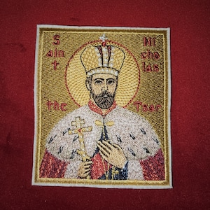 Może przedstawiać: Naszywka haftowana przedstawiająca ikonę religijną mężczyzny z koroną i brodą, trzymającego krzyż. Tło jest złote z tekstem "Święty Mikołaj Car".
