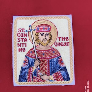 May include: Embroidered patch featuring an image of St. Constantine the Great, holding a cross. The patch has a cream-colored background with gold trim and text. The saint is depicted with a halo, wearing a red and blue robe.