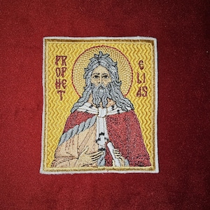 May include: Embroidered patch featuring a religious icon of a bearded man with a halo, wearing a red and white robe. The text "PROPHET ELIJAS" is embroidered around the icon.