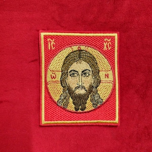 Peut inclure: Un patch brodé rouge avec une bordure dorée représentant une image stylisée de Jésus-Christ. L'image est entourée d'un cercle doré avec les lettres "IC XC" dans les coins.