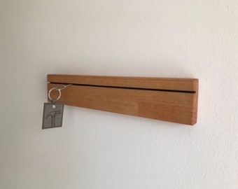 Può includere: Un porta chiavi in legno con una linea nera sul davanti. Una chiave d'argento con un ciondolo a martello è appesa al porta chiavi.