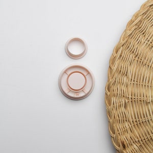 May include: Two plastic curtain rings, one larger than the other, both in a light pink colour. The rings are on a white surface.