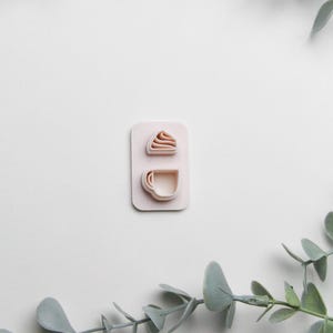 May include: A pink plastic cookie cutter set with two shapes: a cupcake and a coffee cup.