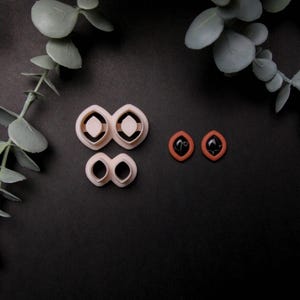 May include: A set of four pink plastic cookie cutters in the shape of diamonds and ovals. Two small red clay earrings with black centers are also shown.