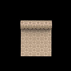 May include: A roll of beige wallpaper with a repeating pattern of square tiles, each containing a carved flower design. The wallpaper is partially unrolled, revealing the pattern. The background is black.