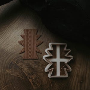 May include: A brown, textured clay object and a white plastic cookie cutter, both in a geometric design, are on a wooden surface. The clay object has a detailed pattern. The cookie cutter is a negative space of the clay object.