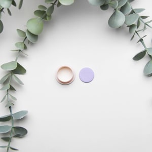 May include: A close-up of a light pink round bottle stopper with a purple round sticker next to it.