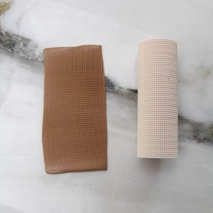 May include: Two textured, rectangular clay pieces. One is a flat, brown rectangle. The other is a cylindrical, off-white shape. Both have a grid-like pattern. The items are on a white and gray marble surface.
